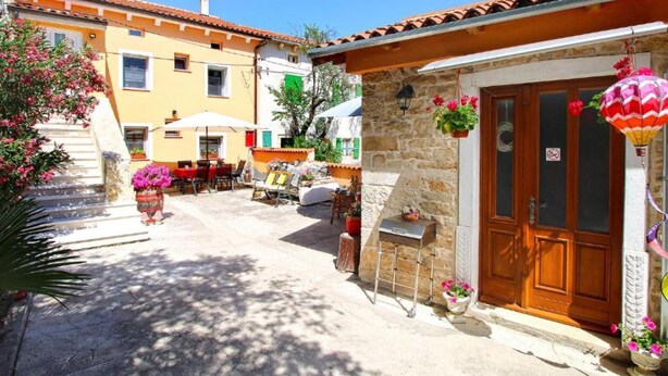 Un patio con mesas al aire libre, un edificio de piedra con una puerta de madera y un farol colgante de colores.