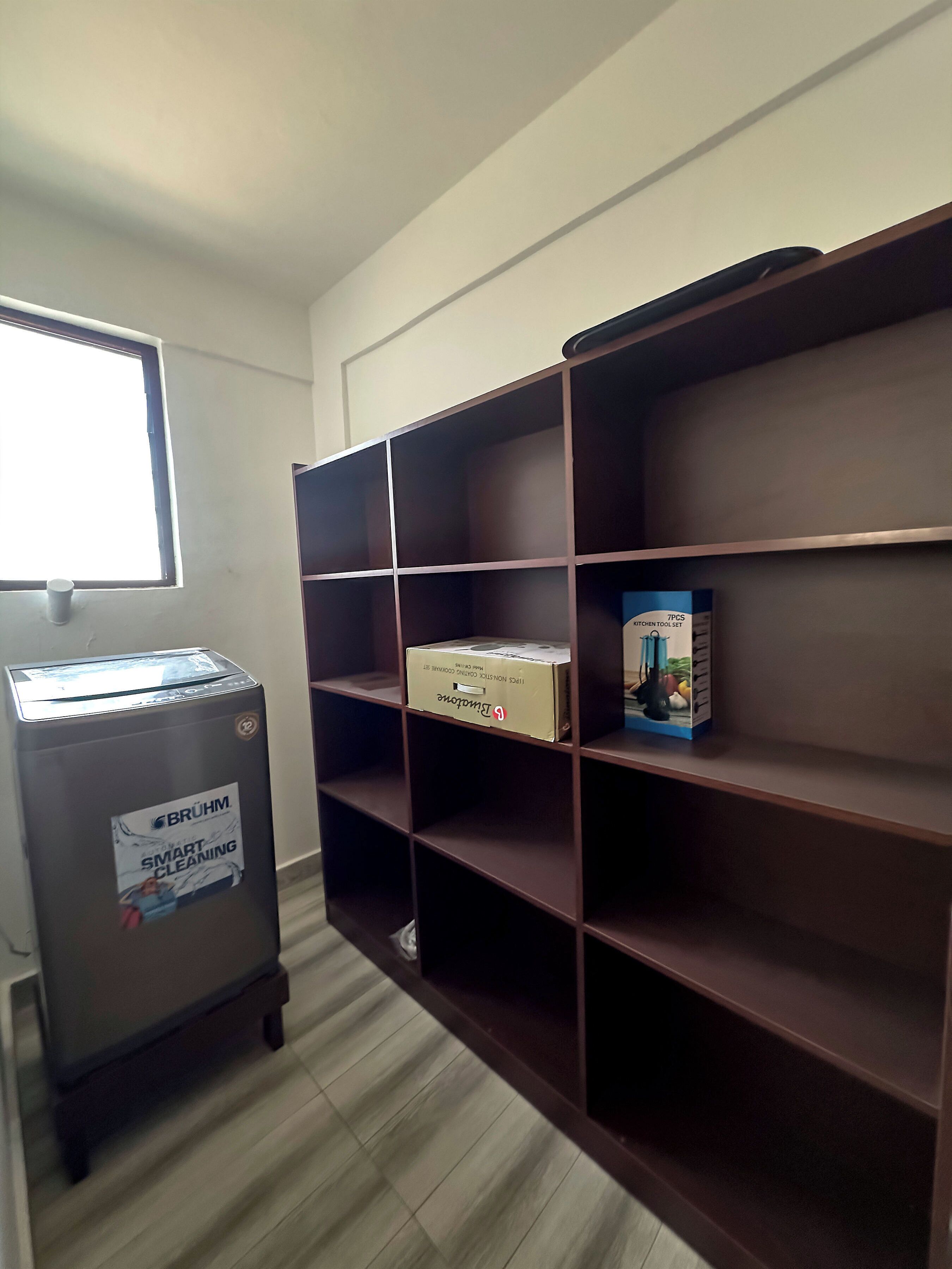 Een kamer met een houten boekenkast, een prullenbak en een raam.