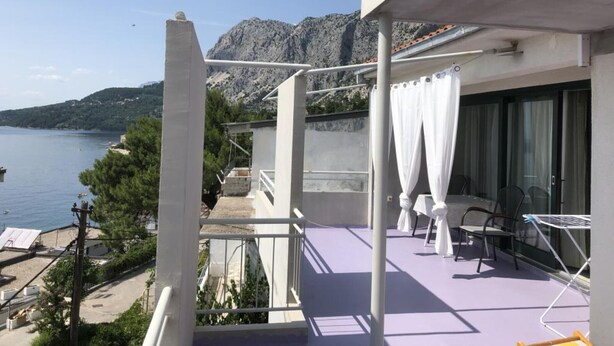 Un balcon avec vue sur la mer et les montagnes, une chaise blanche et une table.
