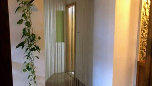 Un couloir avec une plante sur la gauche, un rideau à rayures et un mur en pierre sur la droite.