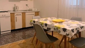 Une cuisine compacte équipée d’une cuisinière, d’un évier et de placards, une table à manger avec des chaises, et un tapis à motifs.