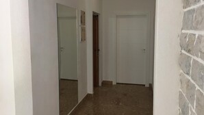Un couloir étroit avec un sol carrelé, une porte blanche et un mur de briques sur la droite.