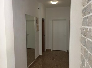 Ein schmaler Korridor mit Fliesenboden, einer weißen Tür und einer Backsteinwand zur Rechten.