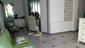 Un salon avec un canapé vert, une petite table sur laquelle est posée une plante, une commode blanche et une fenêtre donnant sur des arbres.