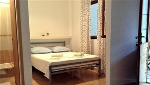 Een slaapkamer met een bed, kussens, een nachtkastje en een raam met gordijnen.