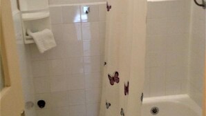 Une salle de bain avec des murs recouverts de carreaux blancs, un rideau de douche orné de motifs de papillons, une serviette blanche posée sur une étagère et une baignoire.