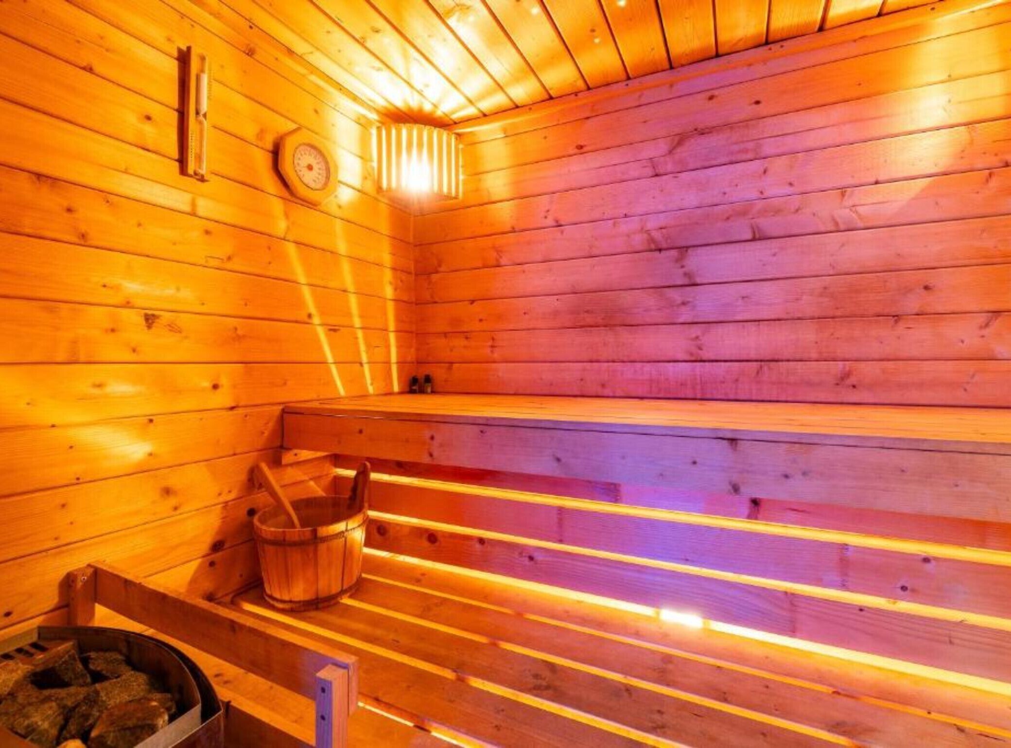 A sauna with wooden benches, a wooden bucket, and a heater.