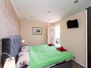 Ein Schlafzimmer mit einem Bett, einer Lampe, einem Fernseher und einer Tür zu einem Außenbereich.