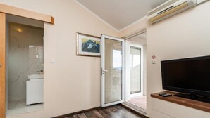 A modern room with a flat-screen TV, a sliding glass door leading to a balcony, and a small kitchenette. - One Bedroom Apartment with Balcony (Sukosan)