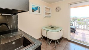A kitchen with a modern stove, a dining area with a table and chairs, a clock, and a balcony with a view. - One Bedroom Apartment with Balcony (Sukosan)