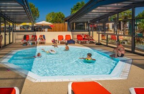 Une piscine avec des personnes, des chaises longues et un espace abrité.