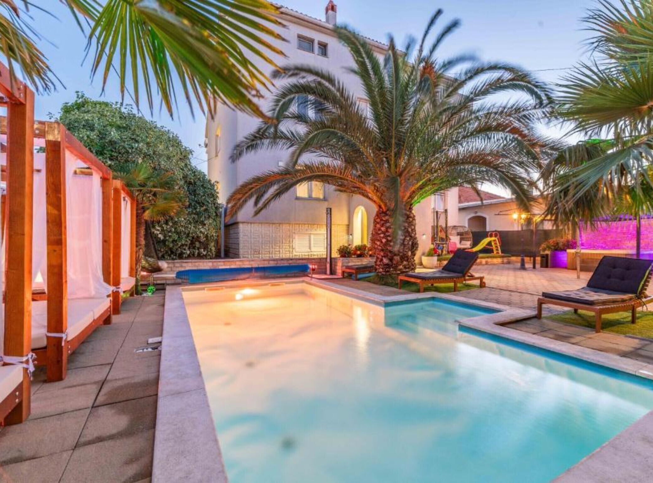 A swimming pool with lounge chairs, palm trees, and a building in the background.