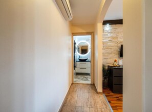 Un pasillo con una cocina moderna a la vista a través de una puerta abierta, que presenta un salpicadero de piedra y un espejo circular sobre el fregadero.