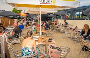 Un café en plein air avec des chaises et des tables en métal, des parasols et une enseigne indiquant « PELFORTH ».