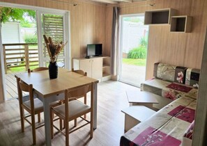 Une pièce comprenant une table à manger en bois, des chaises, un canapé, un téléviseur posé sur un meuble et une porte-fenêtre coulissante donnant sur un jardin.