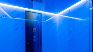 An elevator with a digital control panel, a glass door, and a blue-lit interior. - Obe Bedroom Apartment with Balcony (Sukosan)