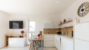 A modern kitchen with white cabinetry, a dining table with chairs, a built-in oven, and a wall-mounted clock. - One bedroom with sea view (Zadar)