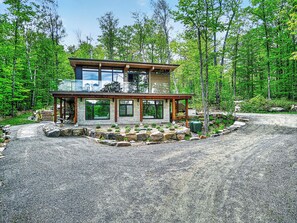 A two-story cabin with a stone foundation, large windows, and a wooden deck. - Vrbo Property (La Conception)