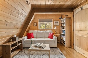 A cozy attic room with a sofa, a table, a lamp, and a bookshelf.
