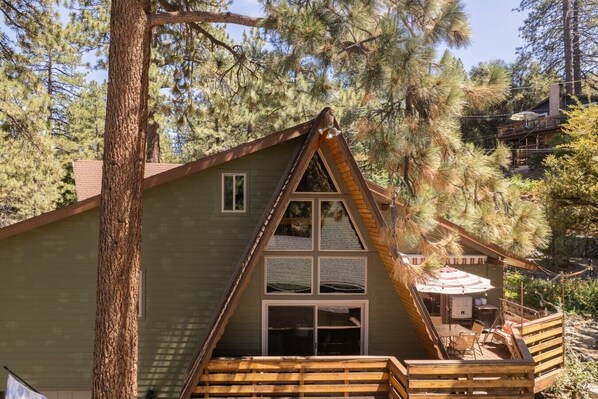 A cabin with a triangular roof, large windows, and a deck with outdoor furniture.