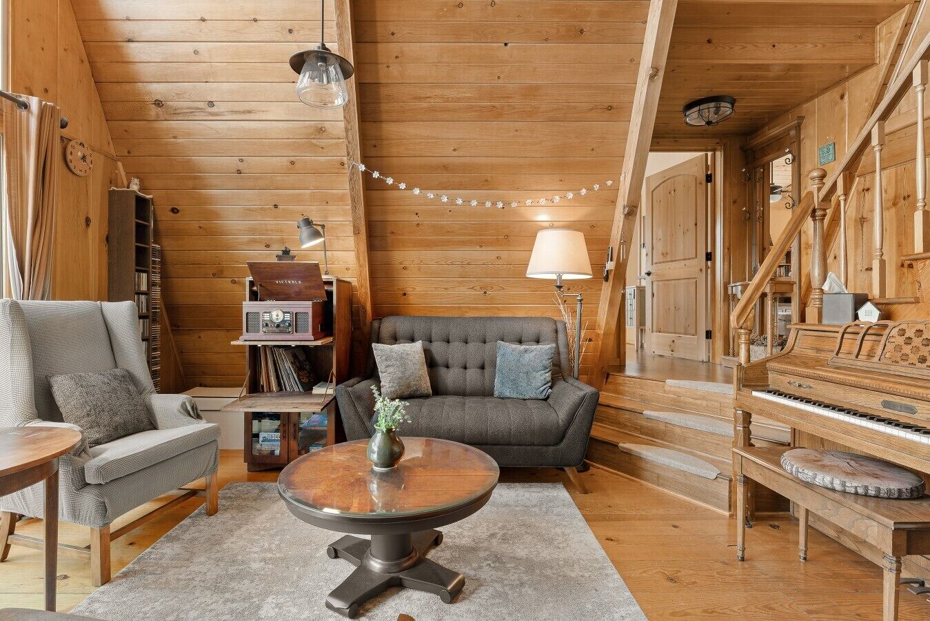 L’intérieur d’un chalet accueillant, avec un plafond en bois, un canapé, un fauteuil, une table, une radio et un piano.