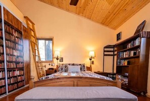 Quarto com uma cama grande, estantes de madeira, uma escada e duas luminárias de cabeceira.
