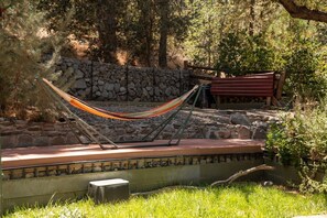 A hammock set up on a stone wall with a bench nearby, surrounded by greenery. - Cloud 9 Cozy A-Frame | Wrightwood Escape (Wrightwood)