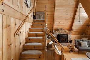 Un intérieur en bois avec un escalier, une cheminée, un canapé et une horloge au mur.