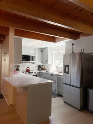 Una cocina moderna con armarios blancos, electrodomésticos de acero inoxidable y techo de madera.