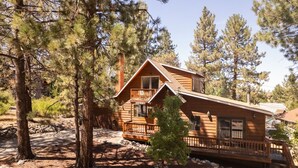 A cabin with a wooden exterior, a balcony, and a small porch. - Pine & Peak | Cozy Cabin Getaway (Wrightwood)