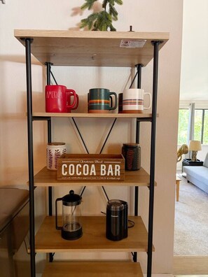 A shelf with mugs, a sign reading 'Cocoa Bar,' and a coffee maker. - Pine & Peak | Cozy Cabin Getaway (Wrightwood)