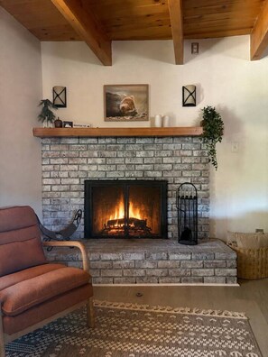 A living room with a fireplace, a chair, a rug, and a plant. - Pine & Peak | Cozy Cabin Getaway (Wrightwood)