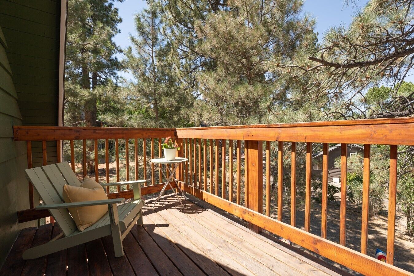 Een houten terras met een bank en een tafel, omringd door bomen.