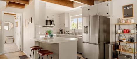 A modern kitchen with a central island, stainless steel appliances, and a wooden ceiling.