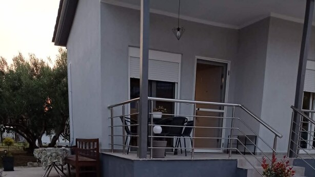 En bygning med balkon, trappe og en lille have med bænk og bord.
