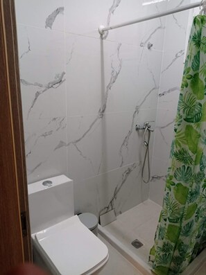 A bathroom with a white toilet, a shower with a handheld showerhead, and a green leaf-patterned shower curtain.