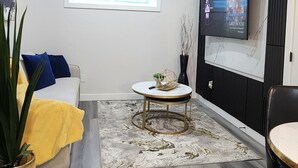 Ein modernes Wohnzimmer mit einer Couch, einem Couchtisch, einem an der Wand befestigten Fernseher und einer Topfpflanze.
