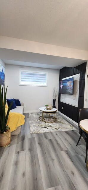 A modern living room with a sofa, a coffee table, a TV mounted on the wall, and a potted plant. - Modern Cozy One Bedroom suite Near WEM (Edmonton)