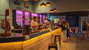 Una zona de bar con mostrador de madera, taburetes y una variedad de botellas y vasos.