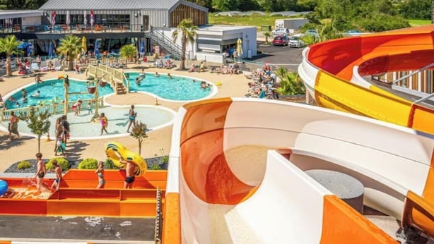 Un parque acuático con varias toboganes y piscinas, rodeado de edificios y árboles.