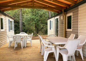 Eine überdachte Terrasse im Freien mit Holzdeck, weißen Plastikstühlen und einem Tisch.