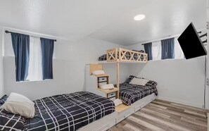 A dorm-style room with bunk beds, a small shelf unit, and a TV mounted on the wall. - Peaceful 5-bedroom Lakehouse in charming Kenai perfect for families (Kenai)