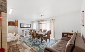 A dining area with a table set for six, a brown leather sofa, and a patterned rug. - Peaceful 5-bedroom Lakehouse in charming Kenai perfect for families (Kenai)