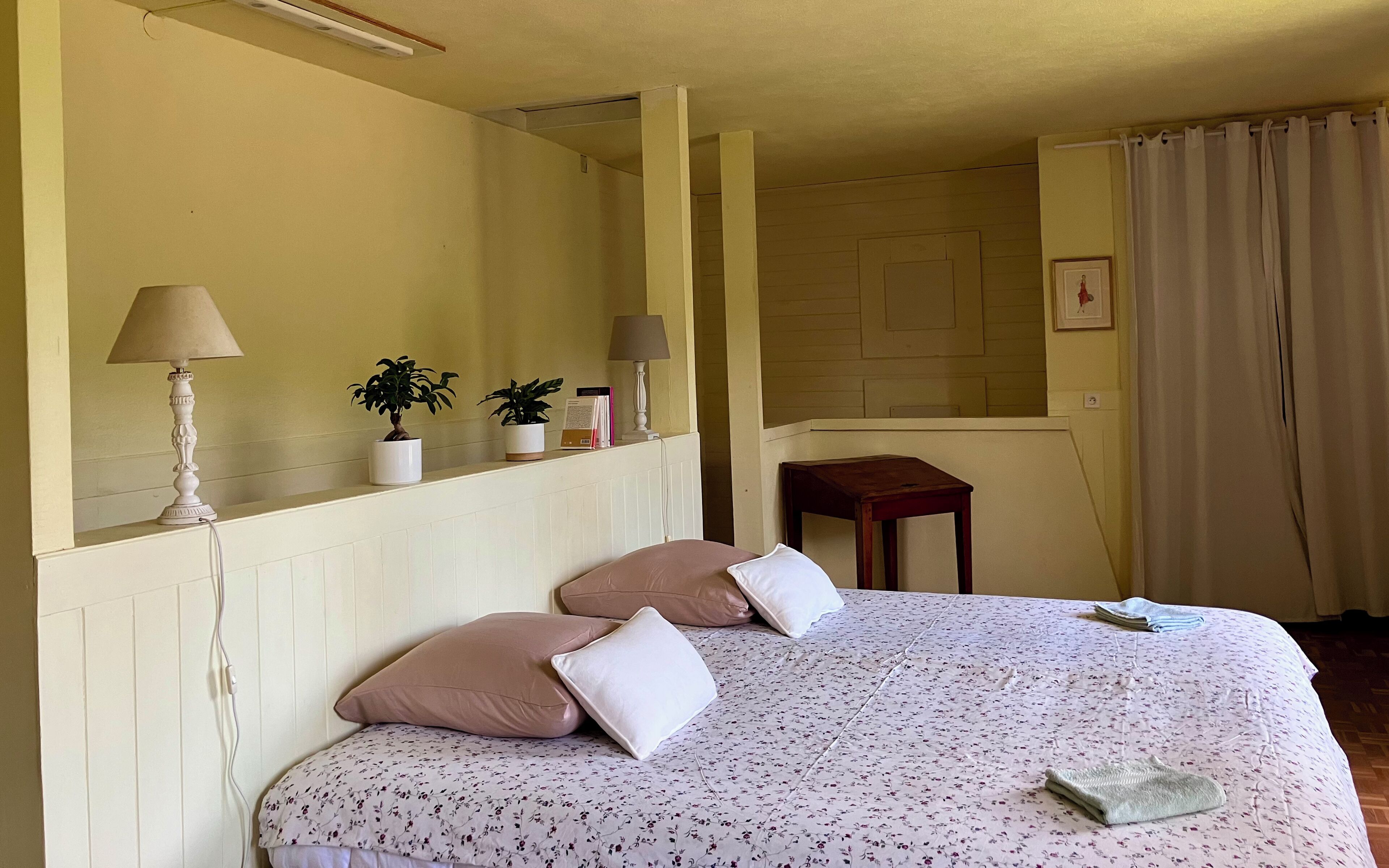 Ein Schlafzimmer mit einem Bett, zwei Nachttischen, einer Lampe, einem Topf mit Pflanze, einem kleinen Tisch und einem Spiegel.