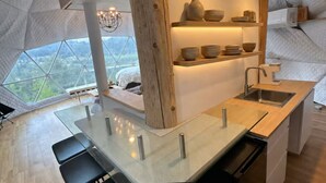 Una cocina moderna con una mesa de comedor de vidrio, detalles de madera y vistas amplias a través de grandes ventanas.