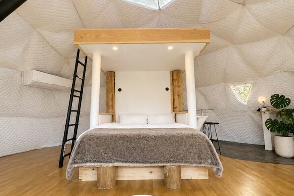 A room with a bed, wooden beams, a ladder, a small table, and a potted plant.