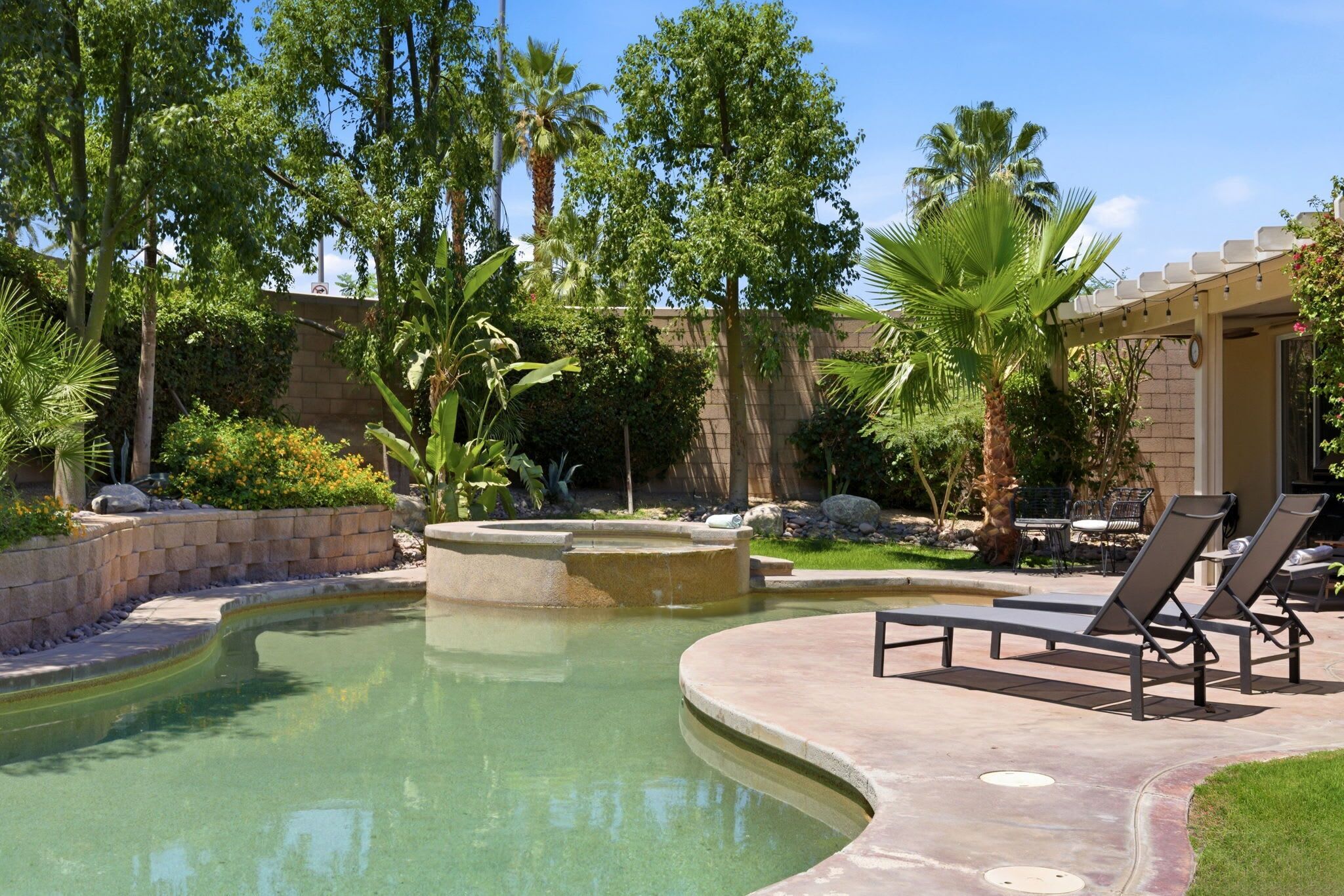 A swimming pool with a curved edge, lounge chairs, and a pergola with outdoor seating.