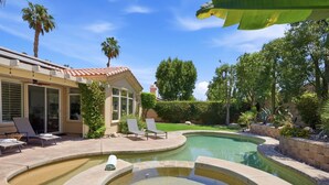 A backyard with a swimming pool, lounge chairs, and a house with a tiled roof. - Palm Desert Pool Home with Mountain Views (Palm Desert)