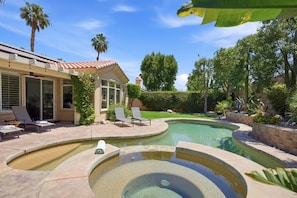 A backyard with a swimming pool, lounge chairs, and a house with a tiled roof. - Palm Desert Pool Home with Mountain Views (Palm Desert)