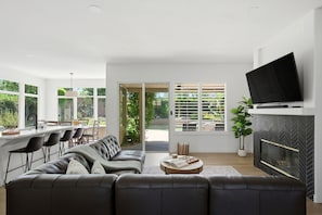 A modern living room with a sofa, a coffee table, a fireplace, and a TV mounted on the wall. - Palm Desert Pool Home with Mountain Views (Palm Desert)